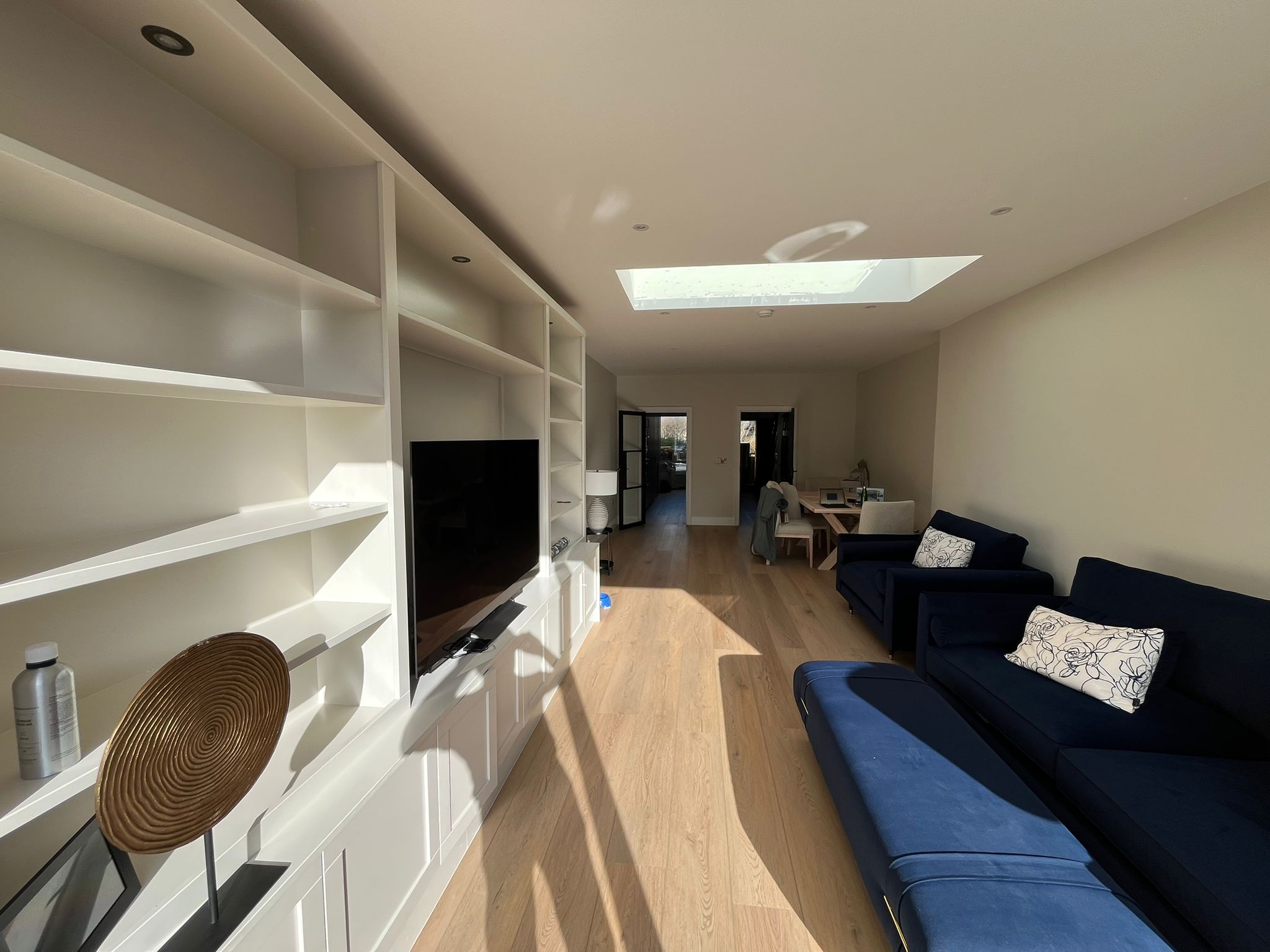 Living room extension with white built-in shelving, TV, blue sofas and skylight - wide angle view