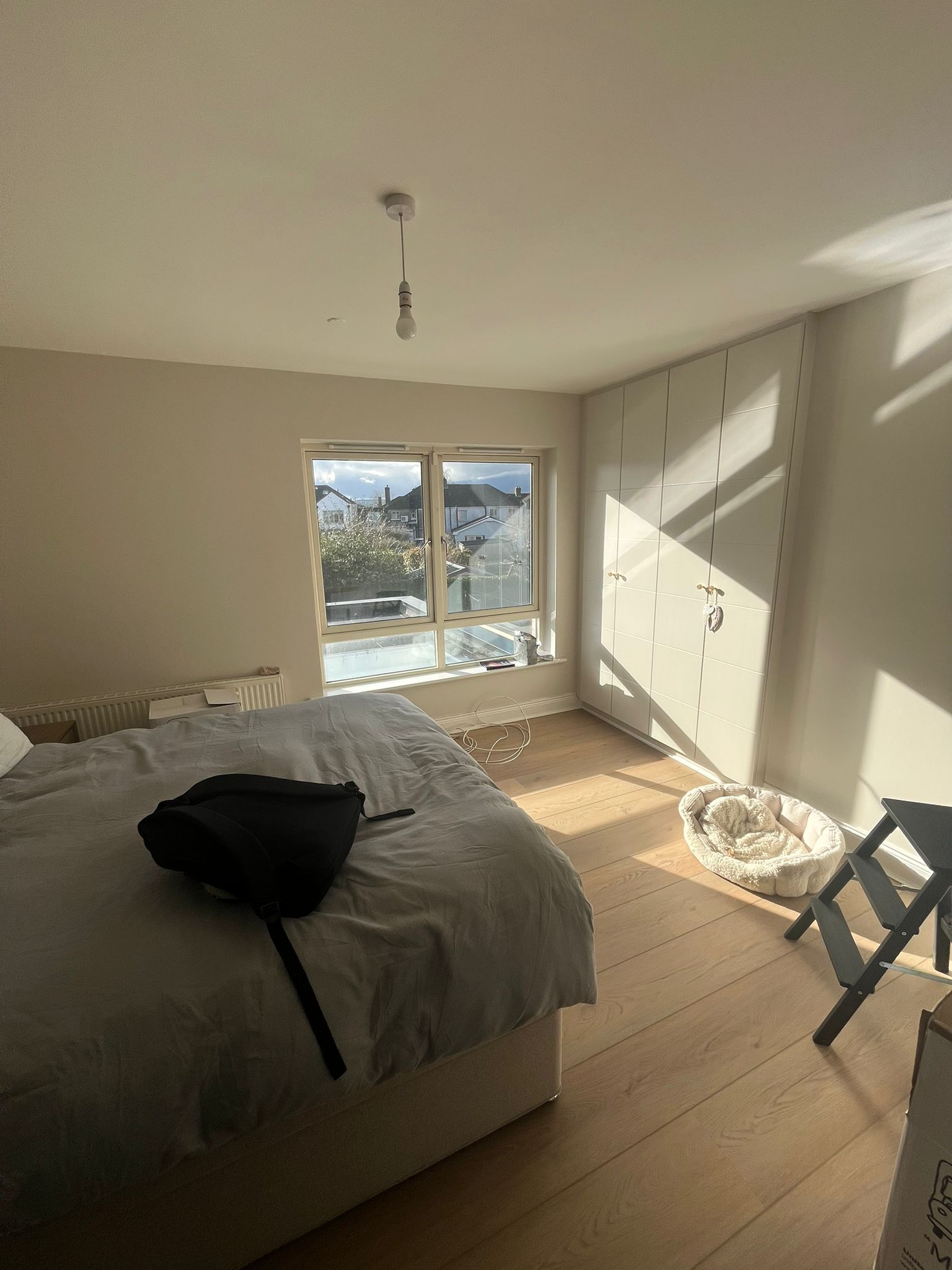 Bedroom with fitted white wardrobe, wooden floors and garden view window