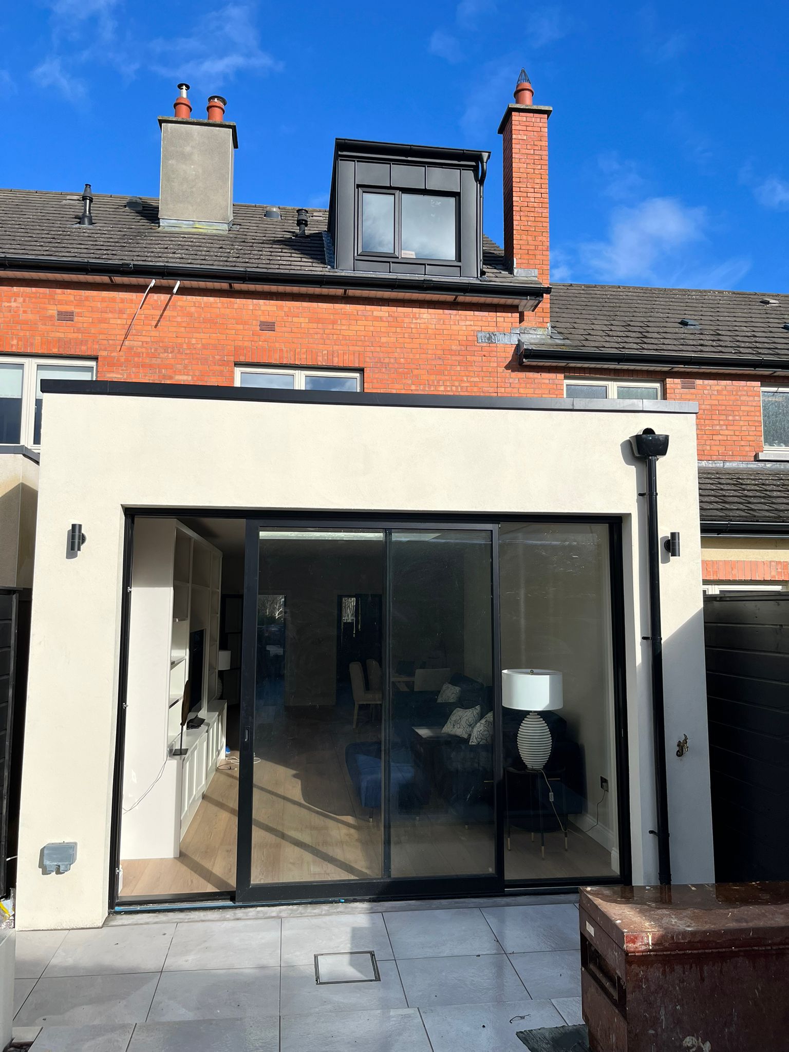 Rear house exterior with white rendered extension, large sliding glass doors and dormer conversion above