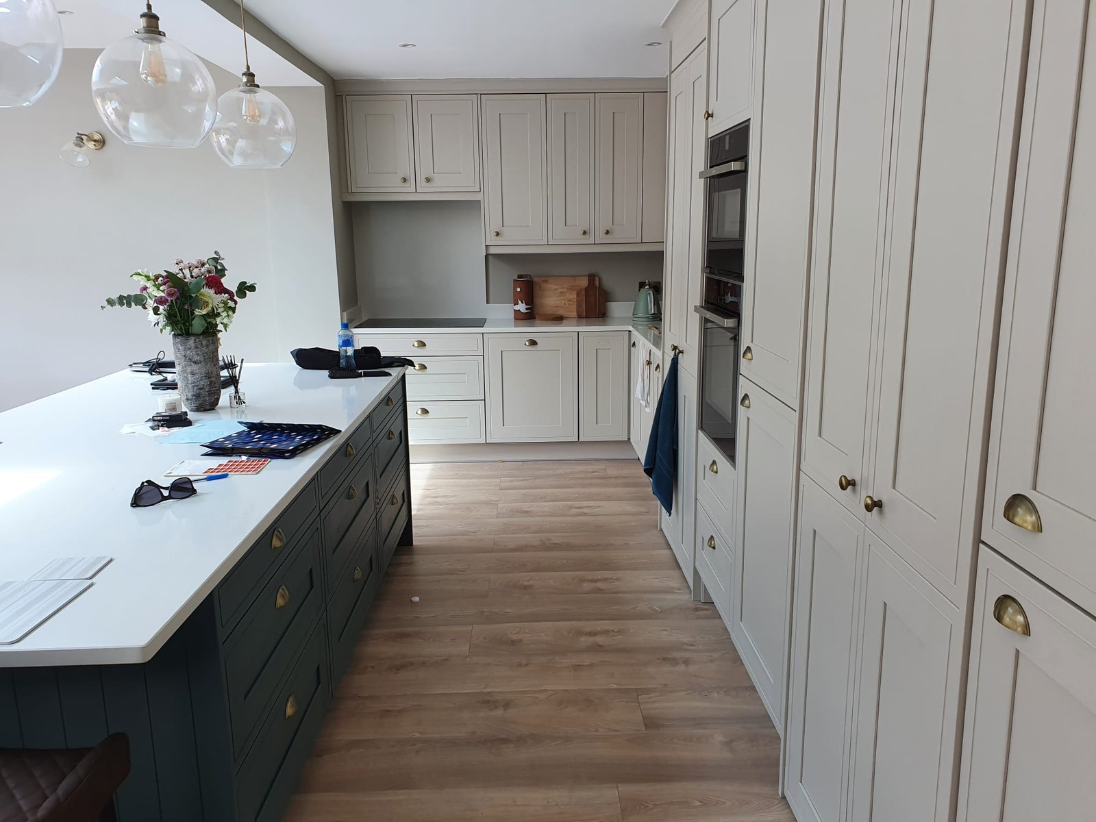 Cream shaker kitchen with dark green island, brass handles and globe pendant lights